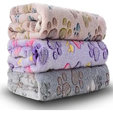 Three folded flannel pet blankets in beige, purple and grey with colourful paw print patterns